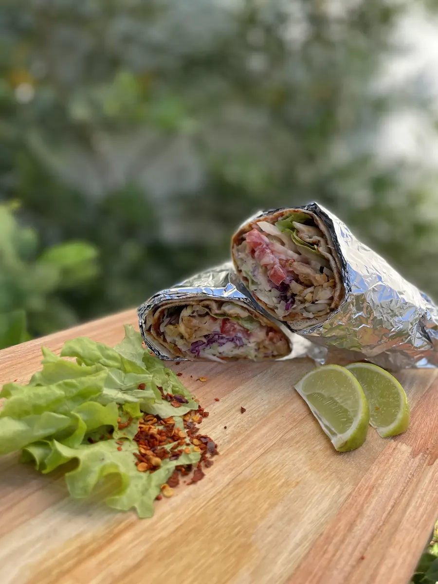 Lahmacun enrollado con ensalada y lima sobre tabla de madera